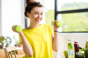 Portrait sports woman yellow t-shirt with dumbbells fresh drinks indoors window background